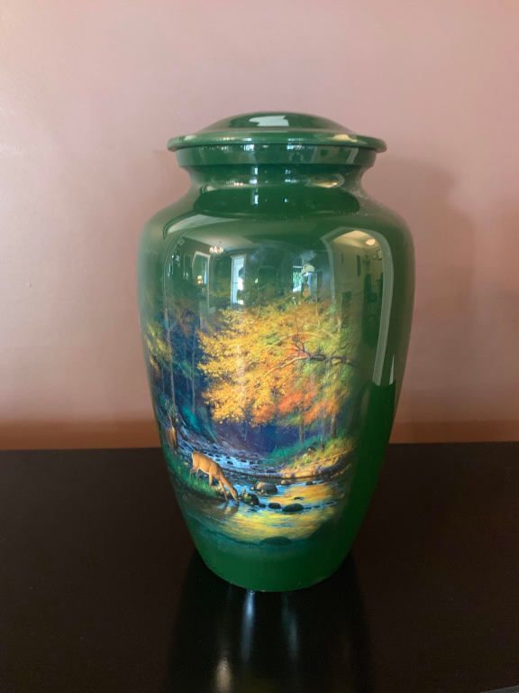 A green urn
with a painting on it is sitting on a table.