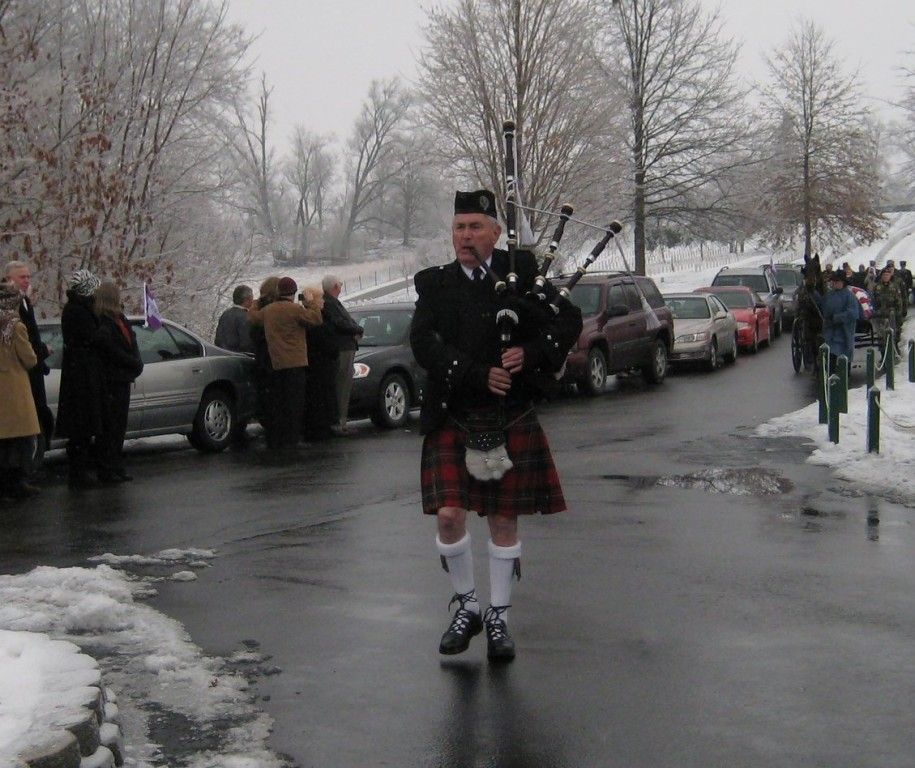 A man in a kilt playing bagpipes in a parking lot