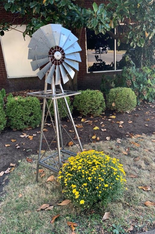 A large windmill is sitting in the grass in front of a building.
