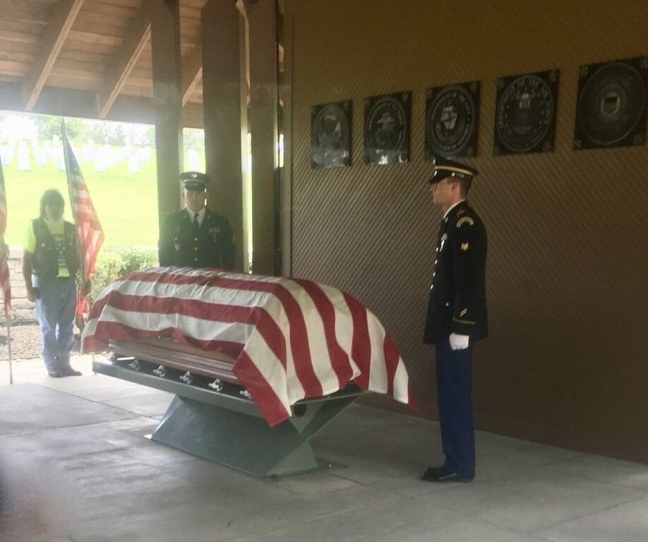 A man in a military uniform stands in front of a coffin covered in an american flag.