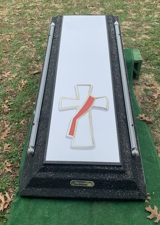 A coffin with a cross on it is sitting on top of a green carpet.