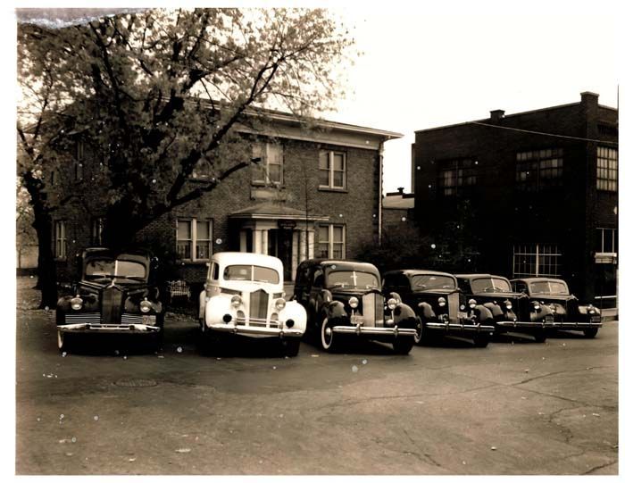 A row of old cars are parked in front of a brick building