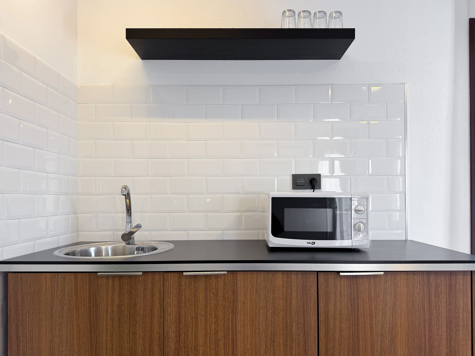 Una cocina con fregadero, microondas y un estante.