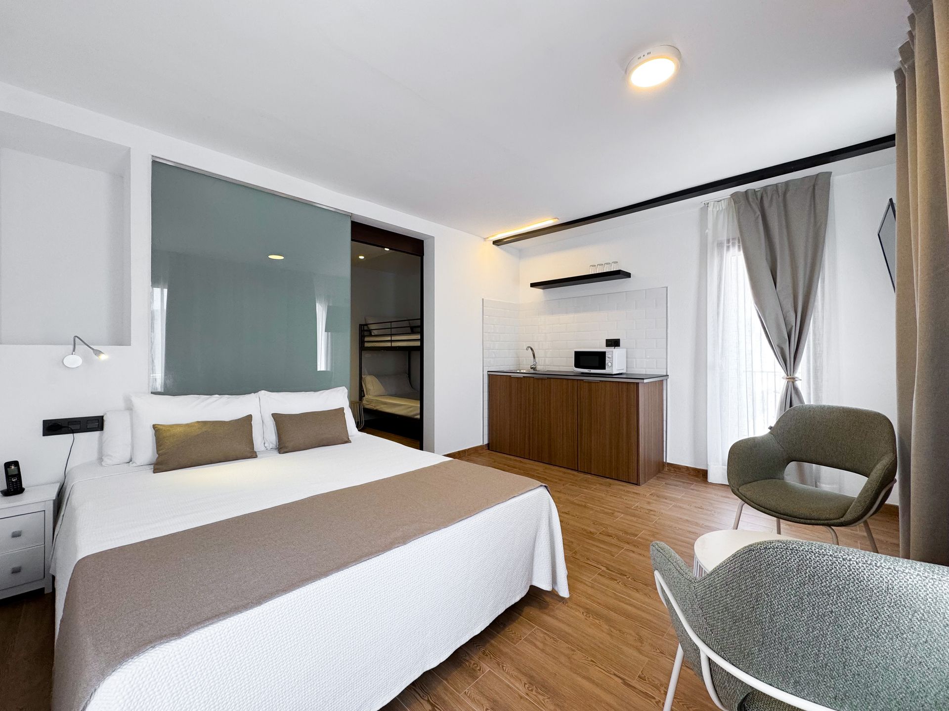 Una habitación de hotel con cama, silla, mesa y cocina.