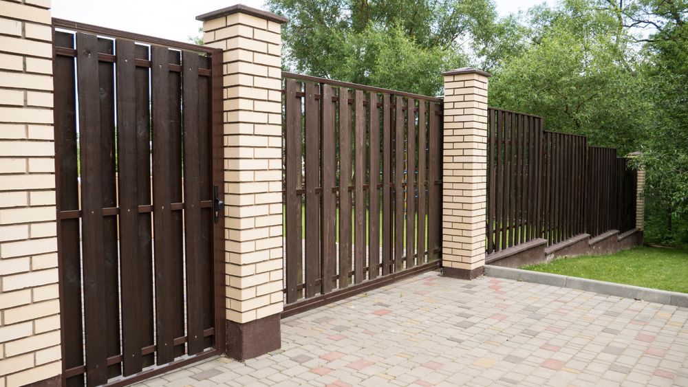 A Brown Wooden Fence With Brick Columns on a Paved — Smiddy's Services In Lake Munmorah, NSW