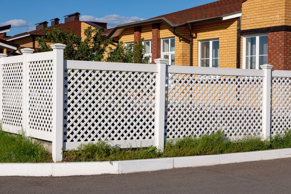 A White Lattice Fence in Front of a Yellow and Brick House — Smiddy's Services In Erina, NSW