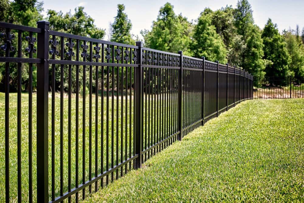 A Black Metal Fence Surrounds A Lush Green Field — Smiddy's Services In Tacoma, NSW