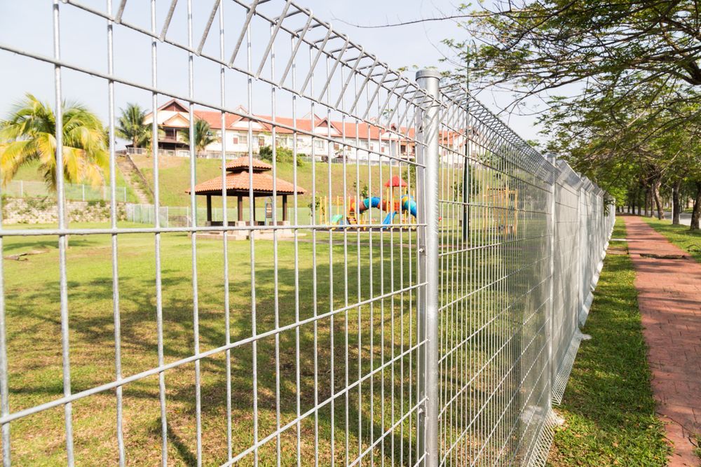 A Metal Fence Encloses a Green Grassy Park — Smiddy's Services In Budgewoi, NSW