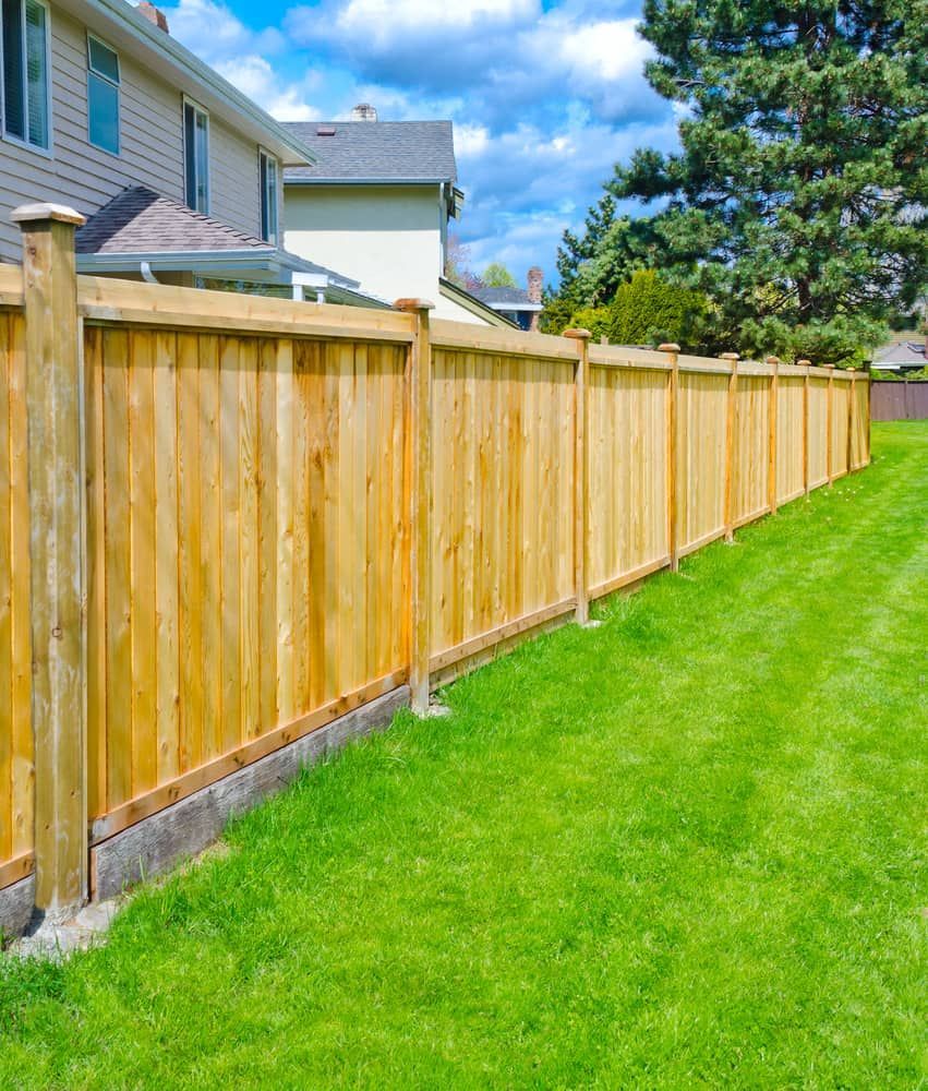 A Wooden Fence Surrounds A Lush Green Lawn In Front Of A House — Smiddy's Services In Tacoma, NSW