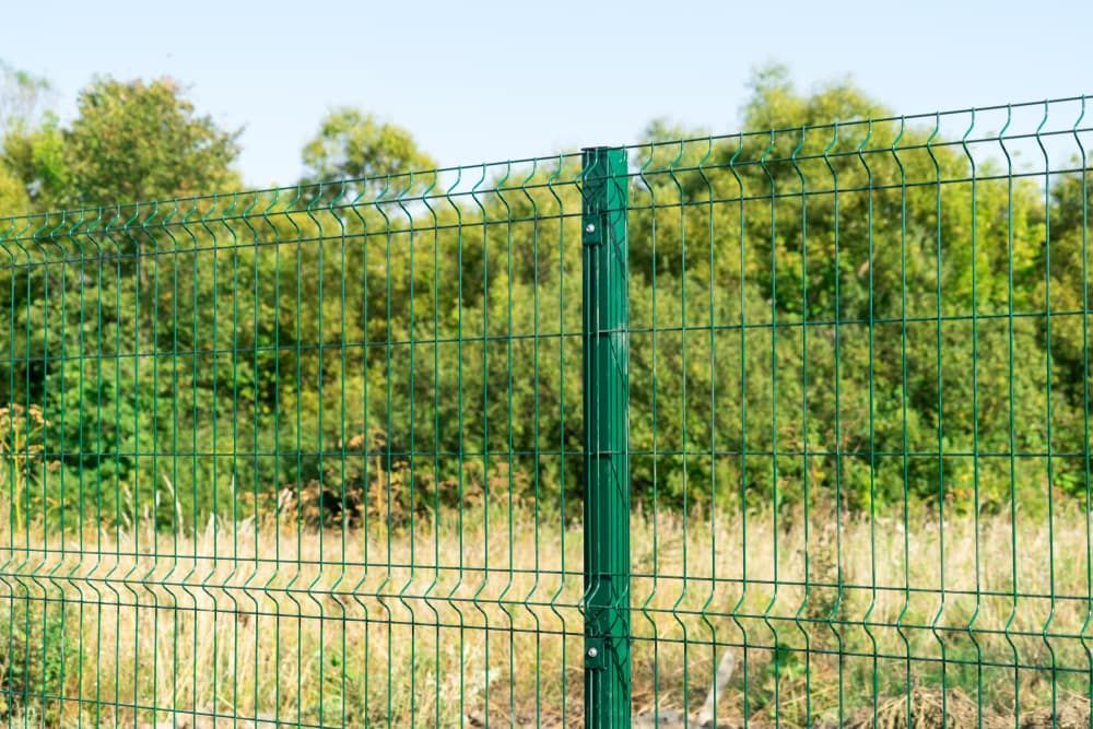 A Green Fence Is Surrounding A Field With Trees In The Background — Smiddy's Services In Gosford, NSW