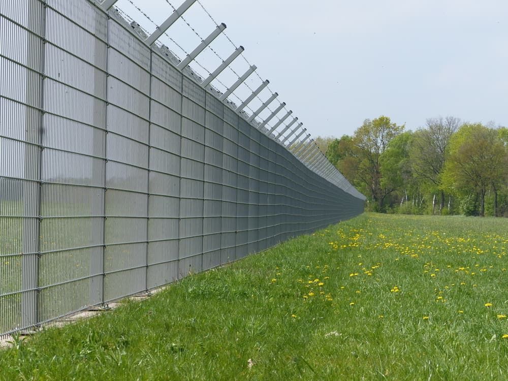 A Fence Surrounds A Grassy Field With Trees In The Background — Smiddy's Services In Tacoma, NSW