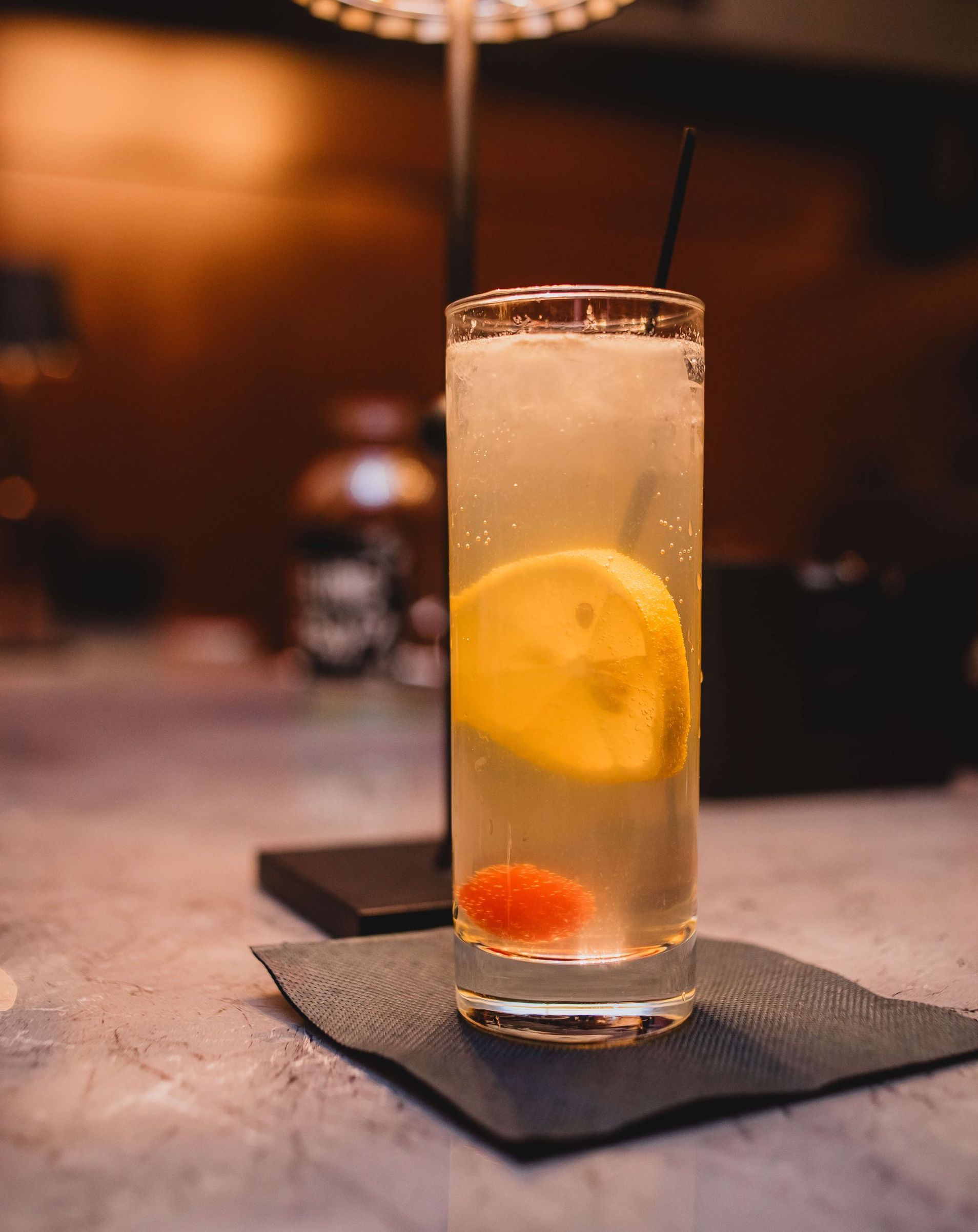 a glass of a vodka collins with a lemon slice with a cherry.