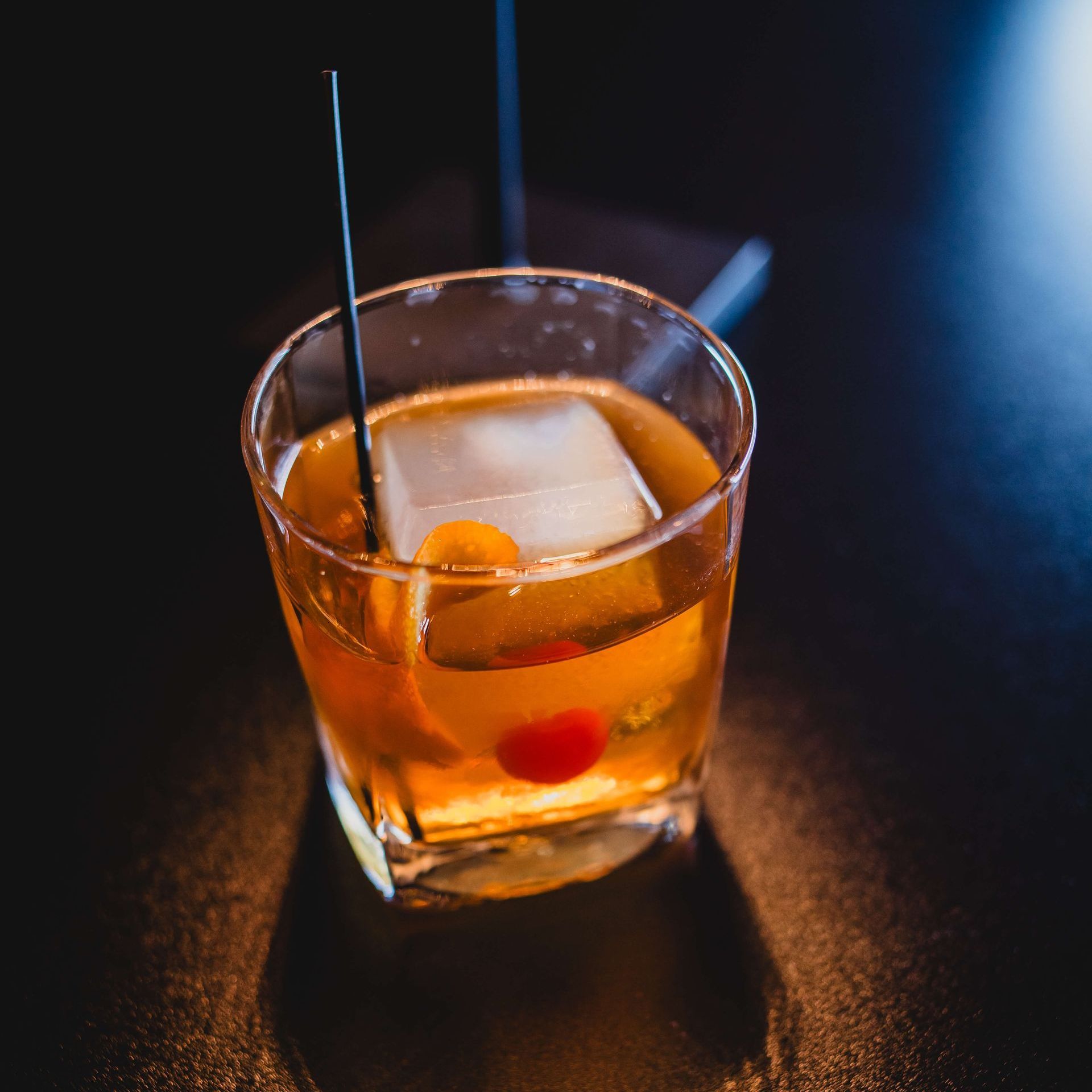 a glass of dark liquid with a slice of orange on a toothpick