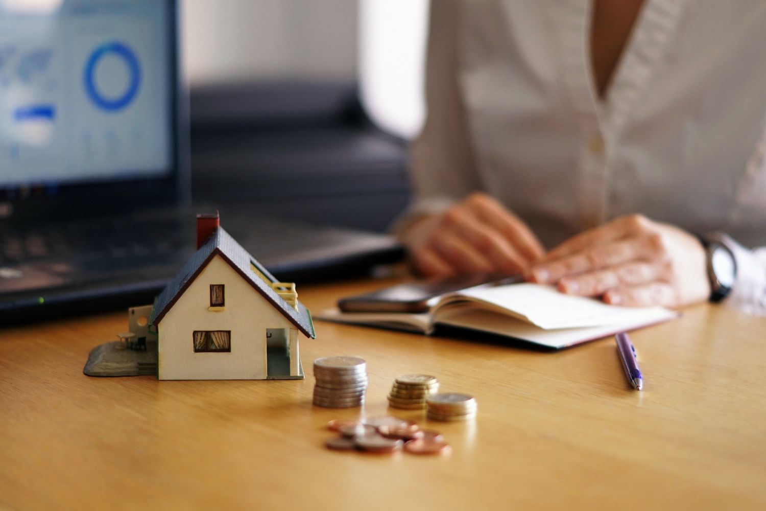 A woman is sitting at a table with a model house and coins.