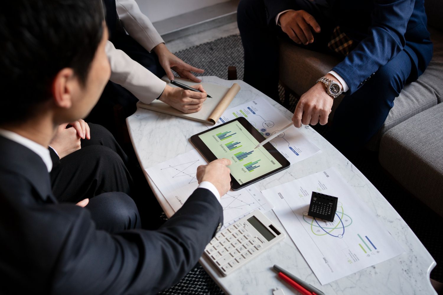A group of people are sitting around a table looking at a tablet.