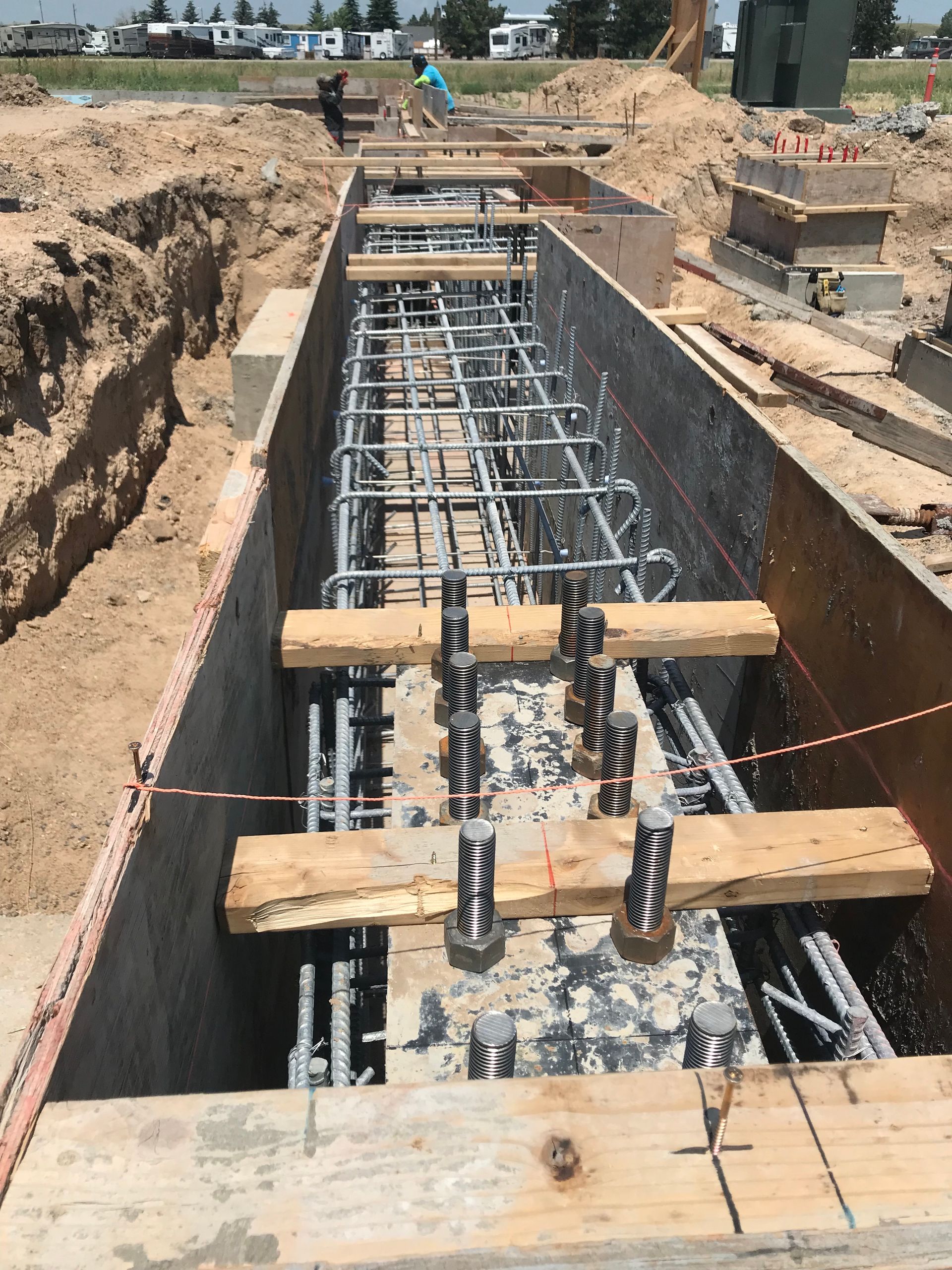 Construction site with several cranes lifting materials to a tall building under construction against a blue sky.