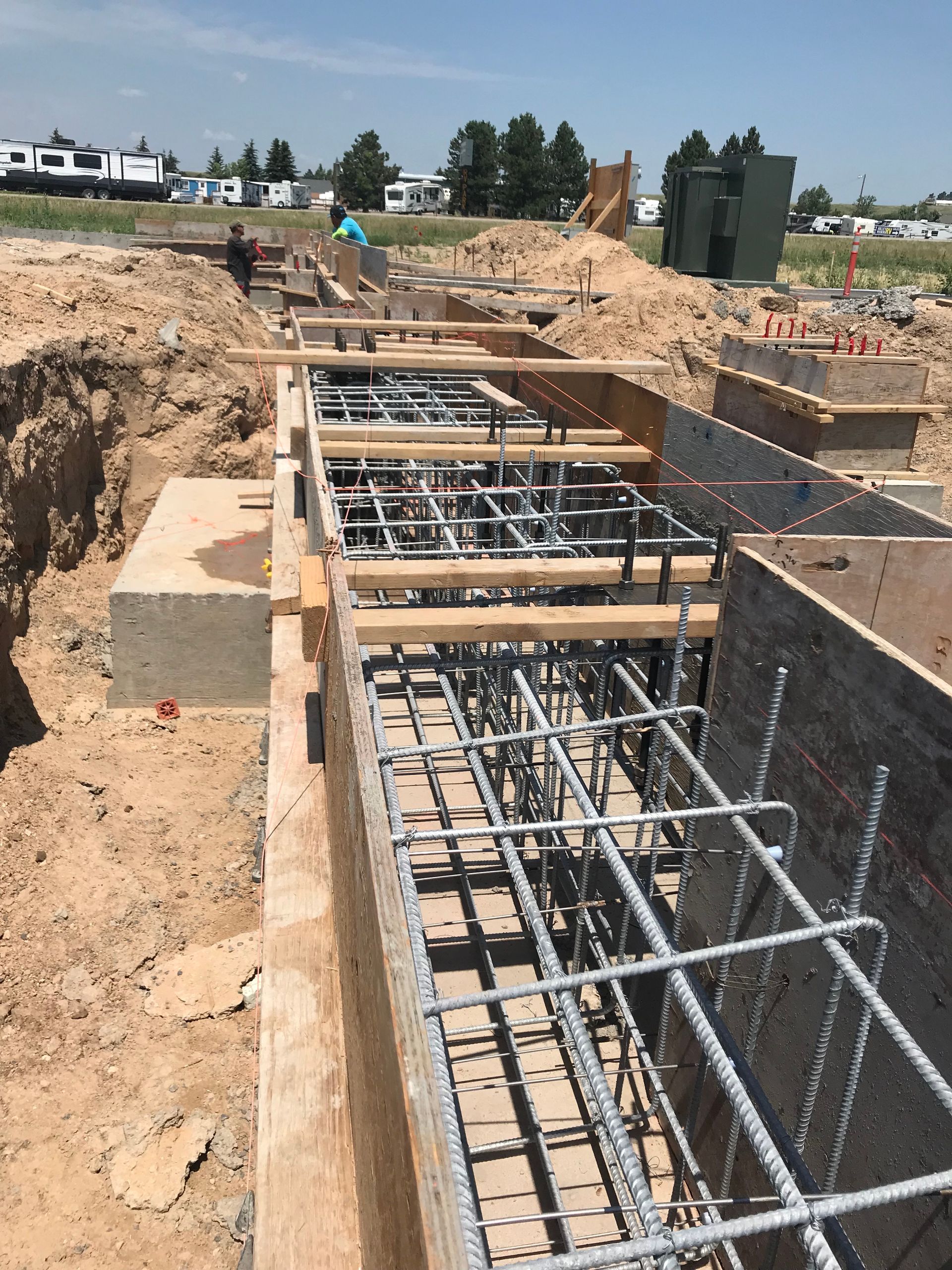 Construction site: Footings with rebar reinforcement within wooden formwork, ready for concrete pouring, on a sunny day.