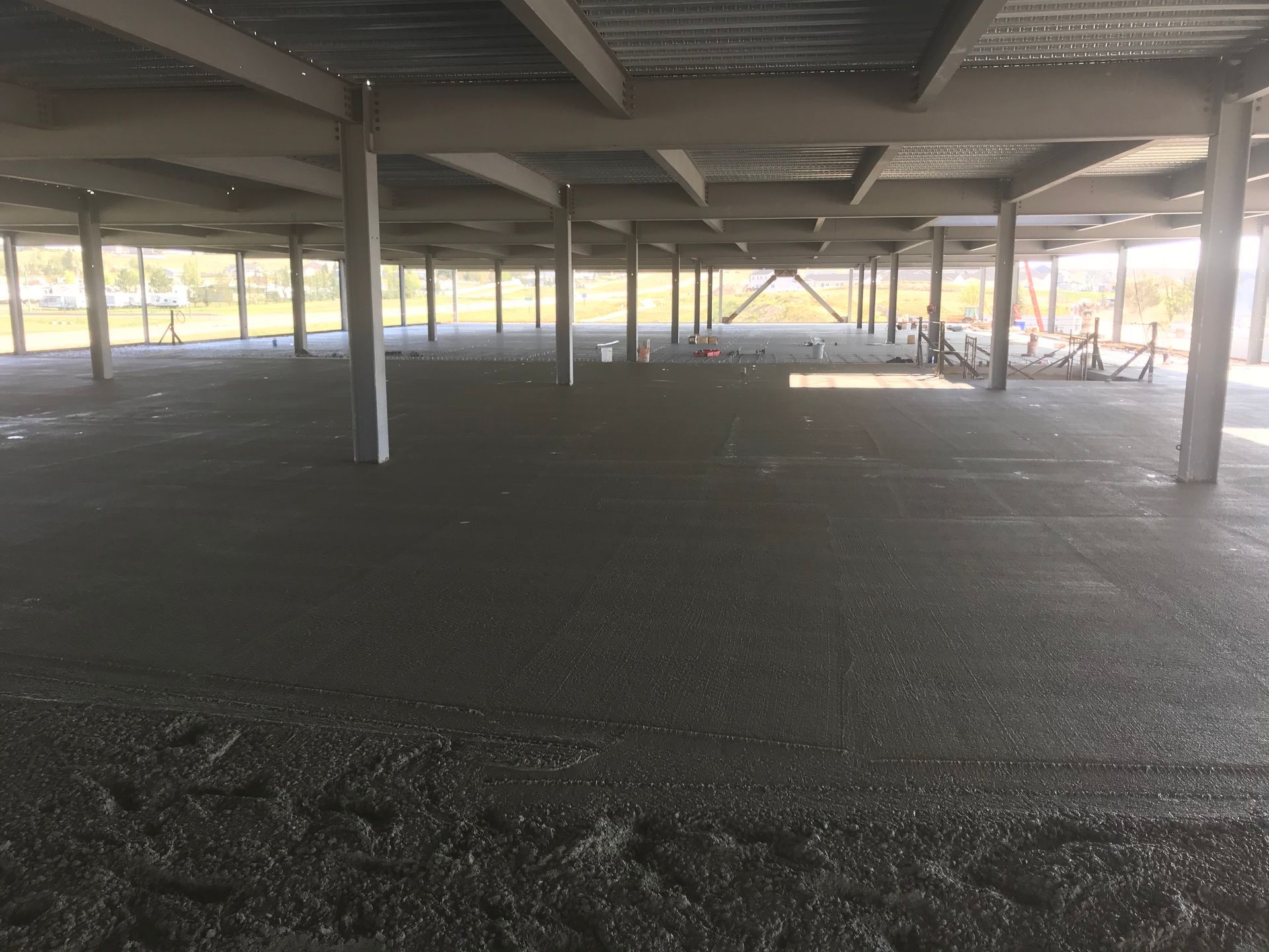 Fresh concrete floor poured inside a steel-framed building under construction, columns support a ceiling.