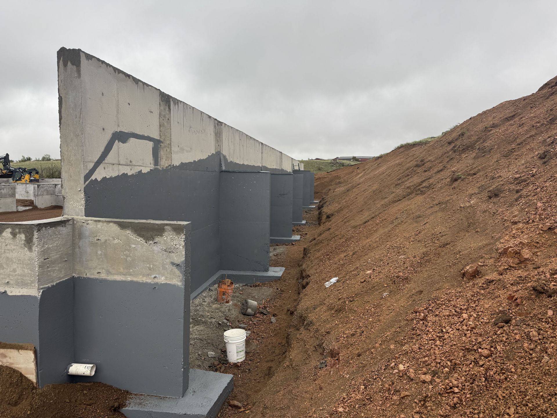 Concrete foundation wall with dark gray waterproofing, next to a dirt hillside.