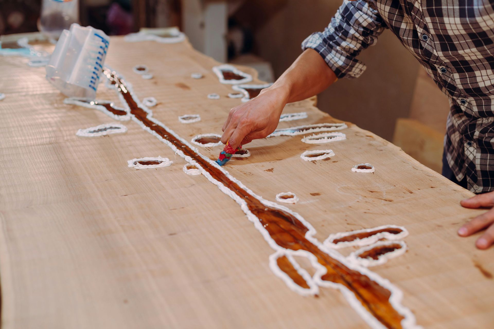Person pouring resin onto a wooden slab, filling cracks and voids.