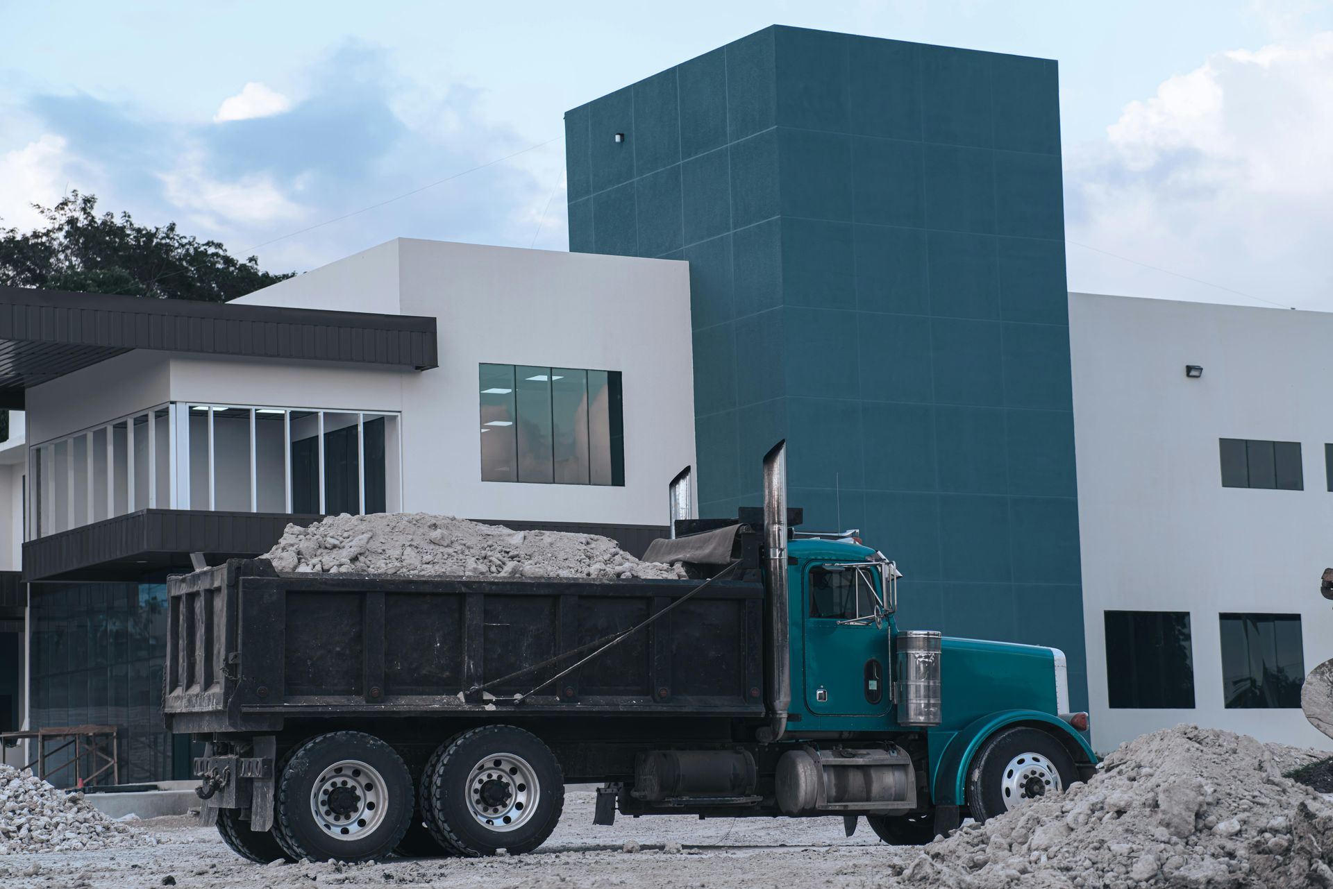 Dump truck loaded with debris parked in front of a modern building under construction; blue and white exterior.