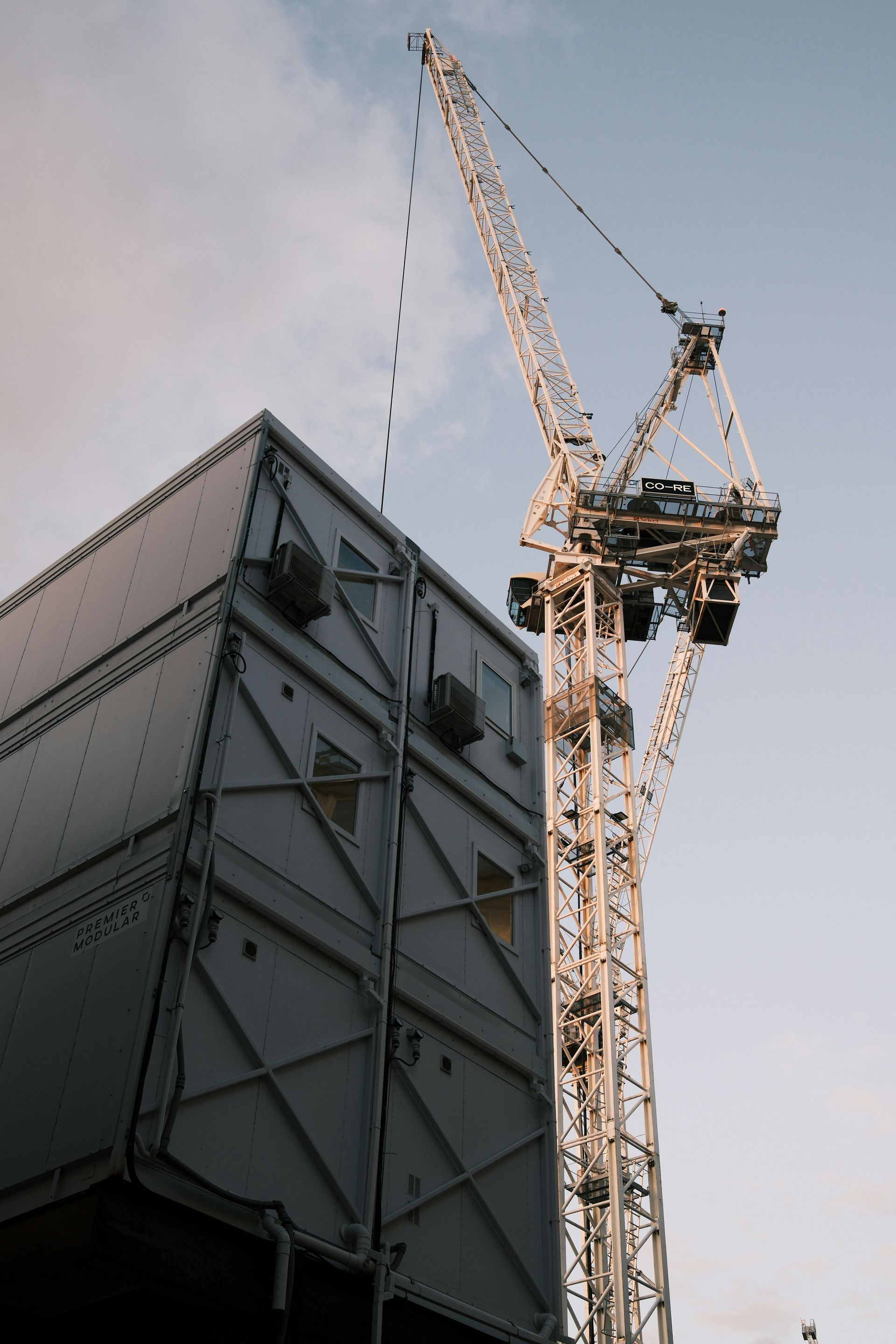 Construction crane next to a metallic, angular building under a pale blue sky.