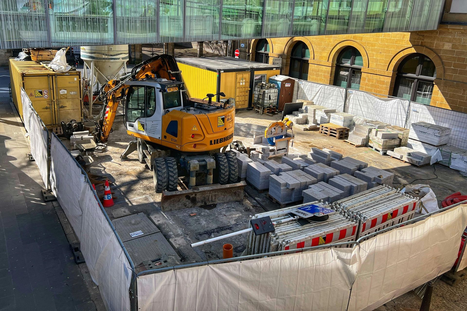 Construction site with an excavator, barriers, and stone blocks.