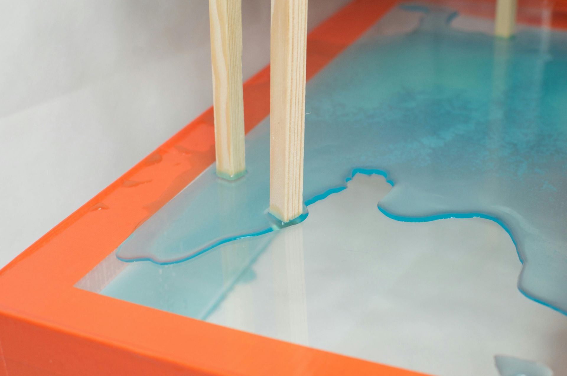 Light-colored sticks in a rectangular orange container filled with blue liquid.