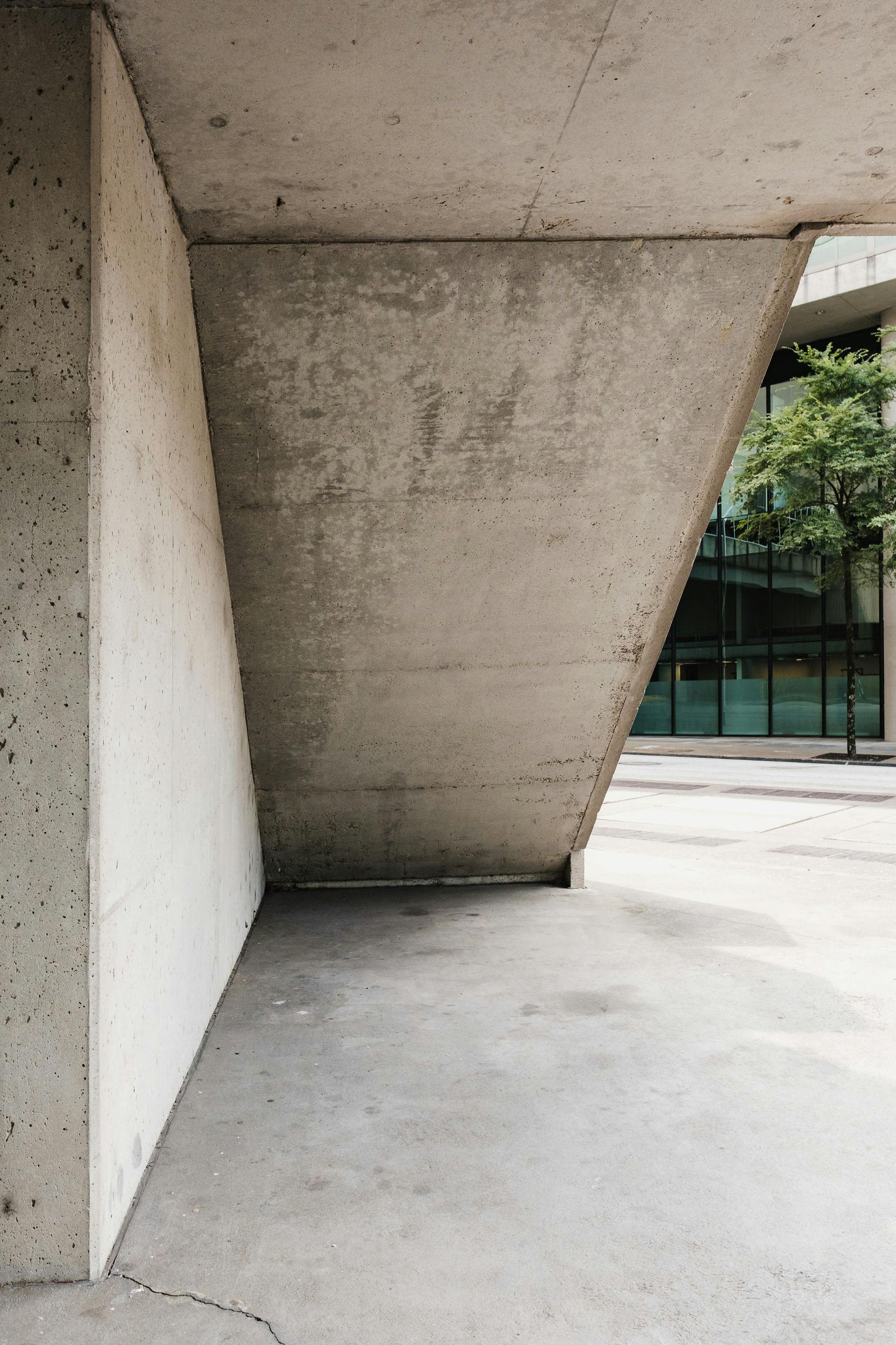 Concrete architectural detail, with a triangular support and view of trees through glass.