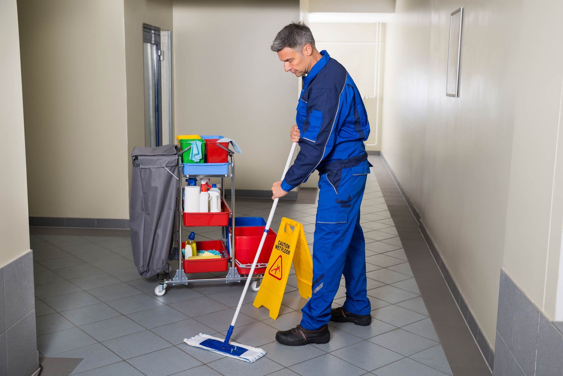 A man is cleaning a hallway with a mop.