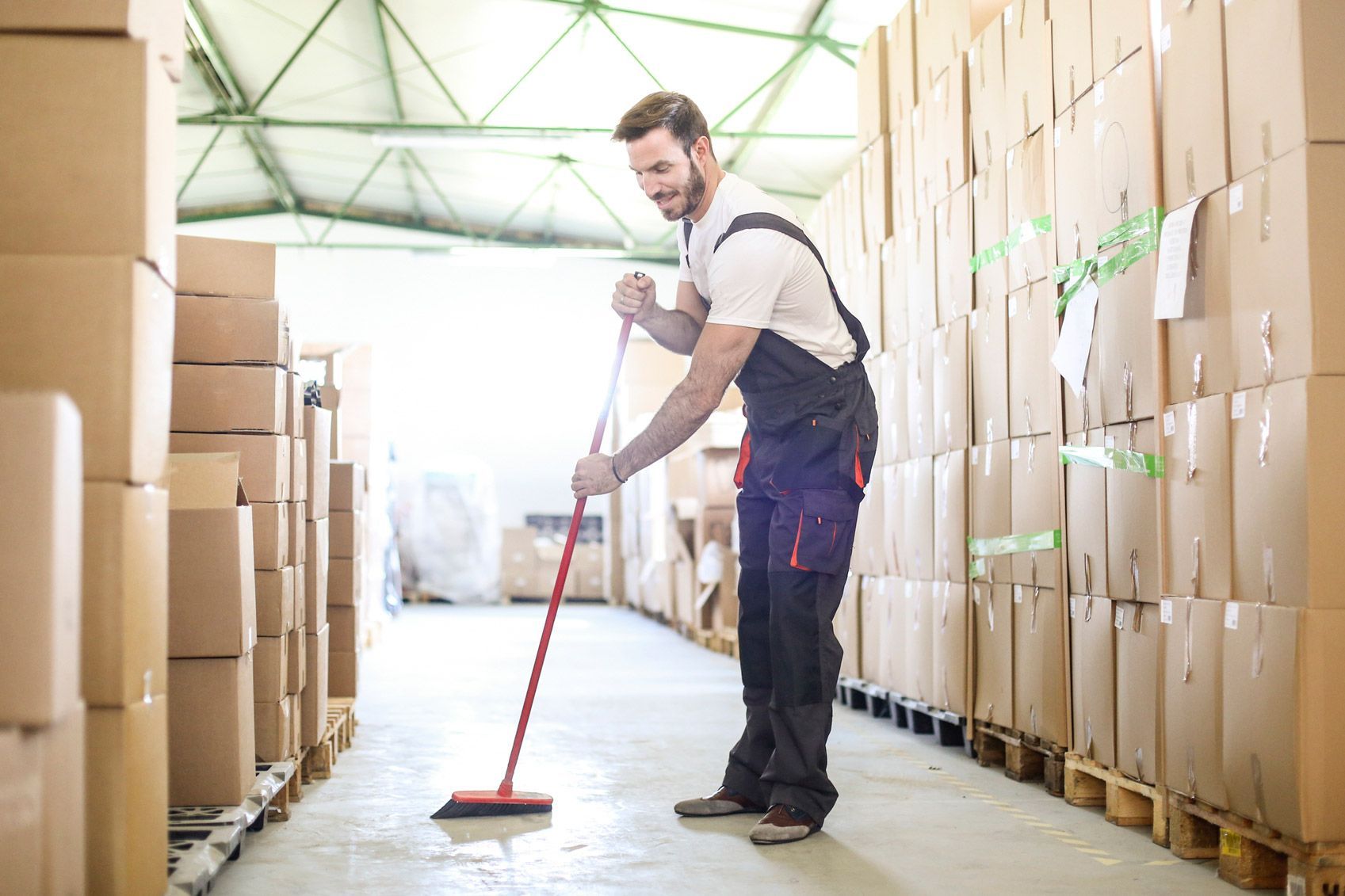 A man is cleaning the floor of a warehouse with a broom.