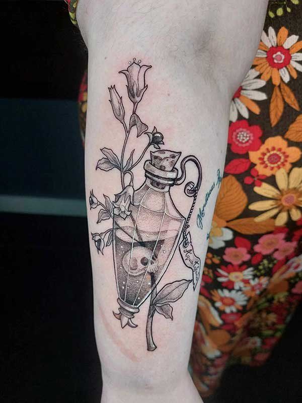 A tattoo of a bottle with flowers and a skull on it