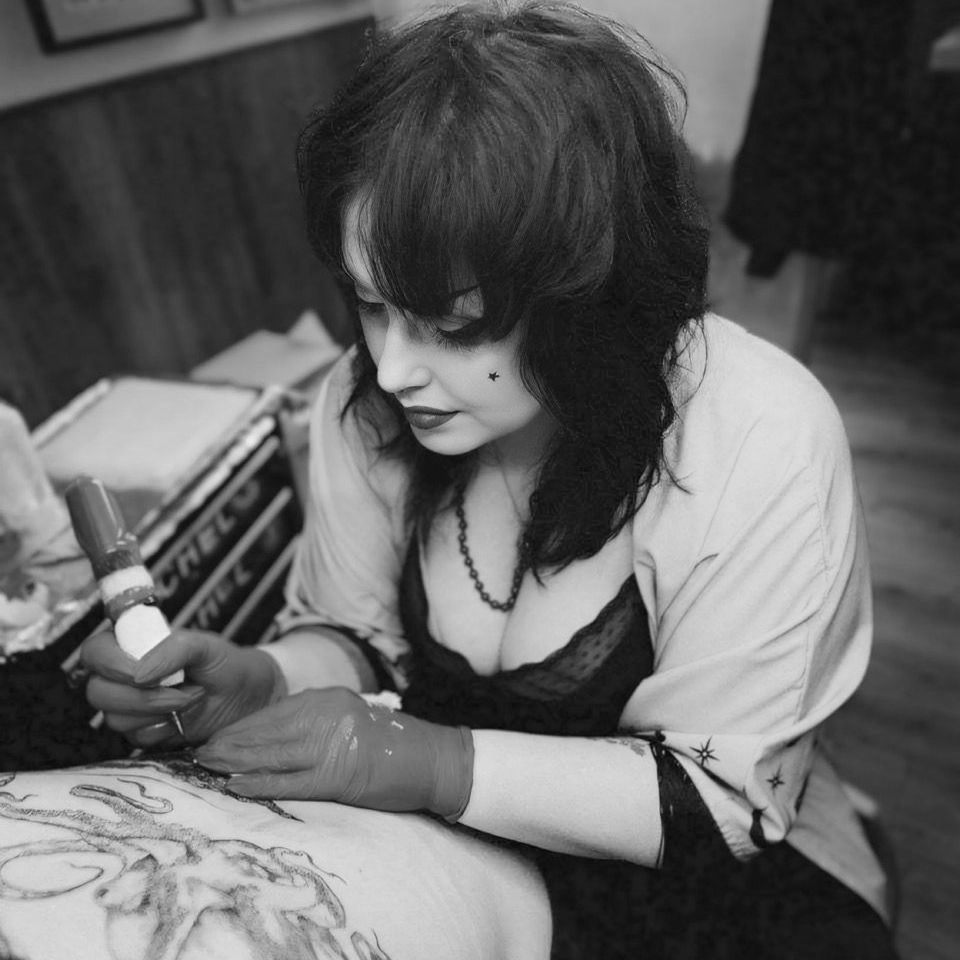 A woman is getting a tattoo on a person 's arm.