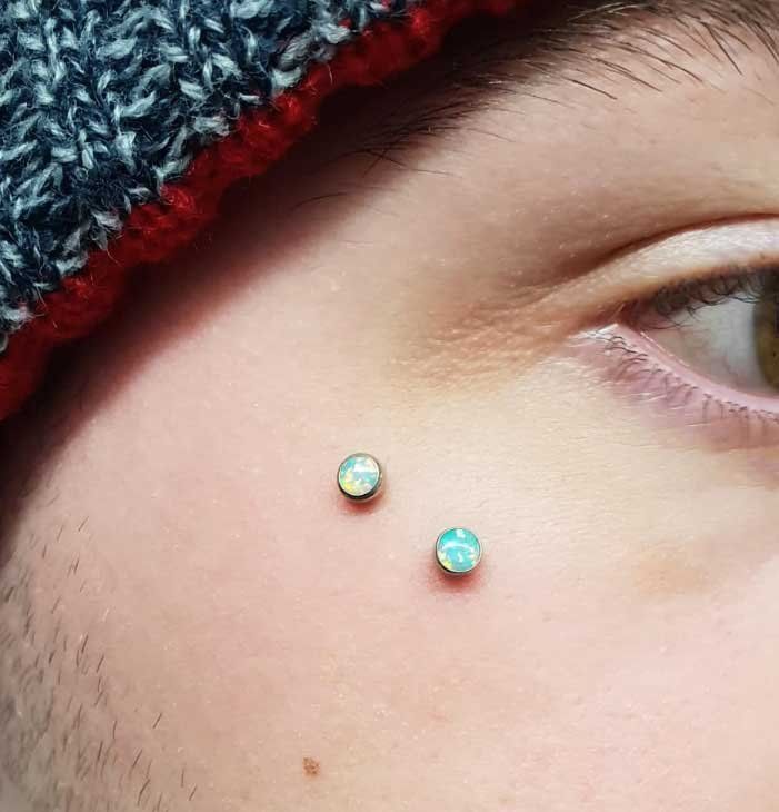 A close up of a person 's face with two piercings on it.