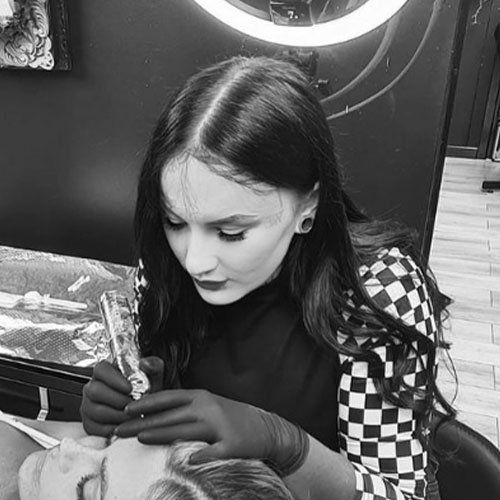 A woman is getting a tattoo on a man 's face in a black and white photo.