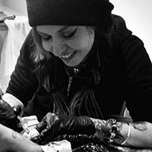 A woman is smiling while getting a tattoo on her arm.