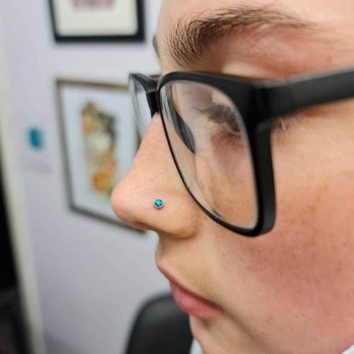 A close up of a person wearing glasses and a nose ring.