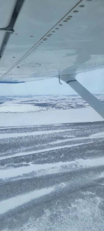 View from a small plane over snowy ground, with the wing and strut visible.