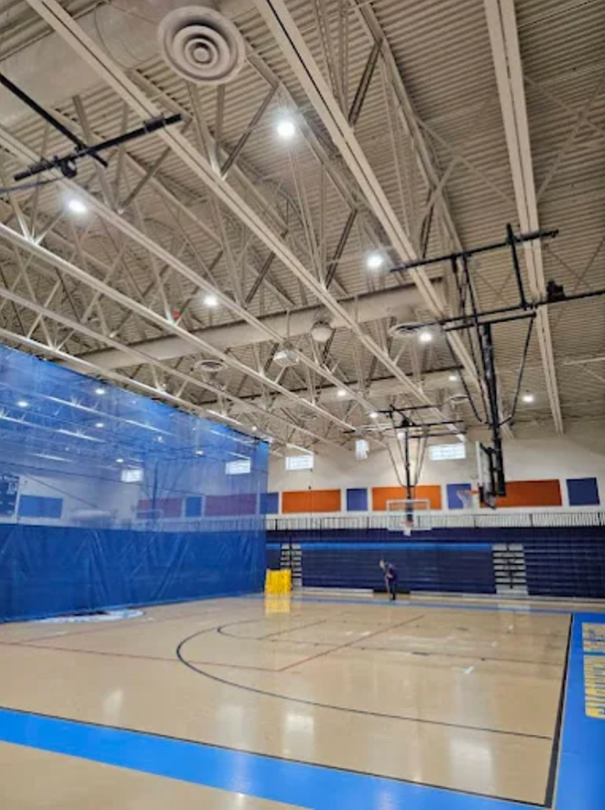 Empty indoor basketball gym with blue padding, bleachers, and bright ceiling lights
