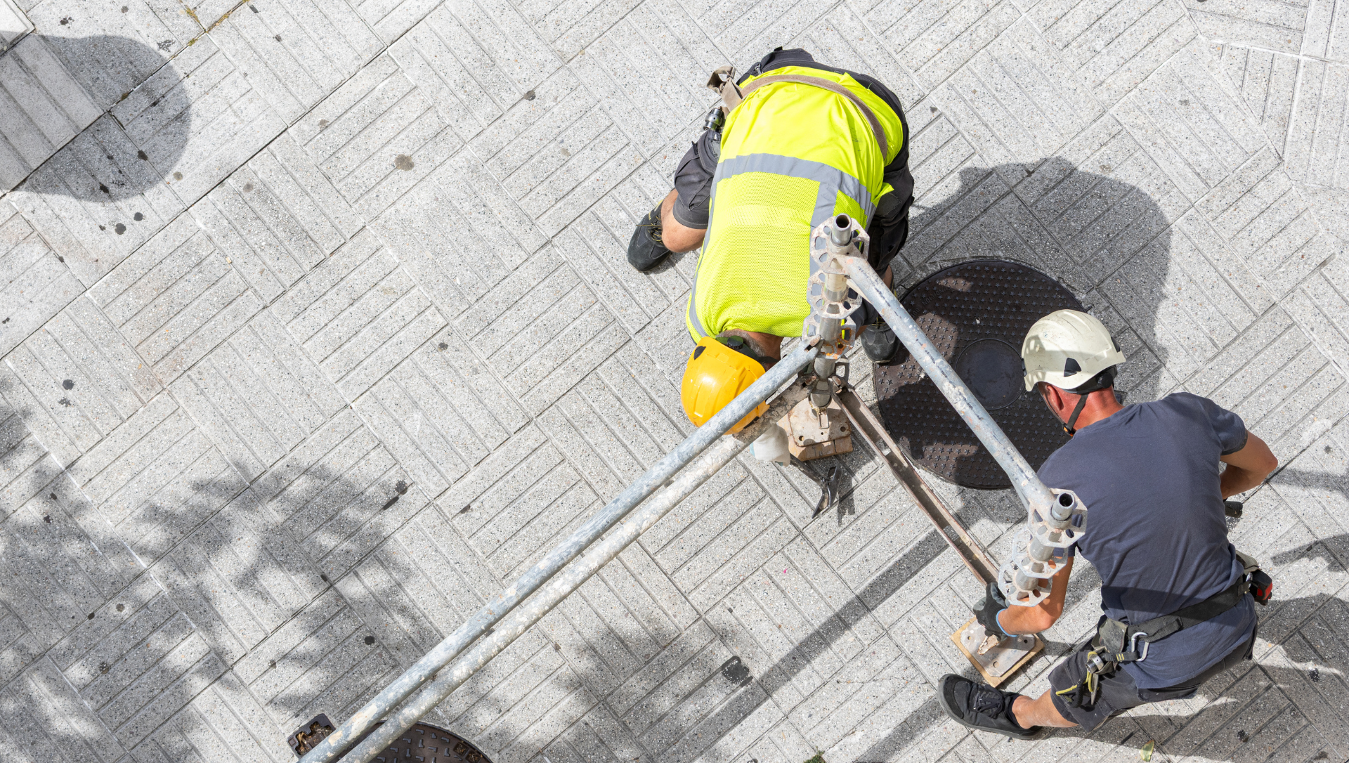 Two workers in safety gear near an open manhole, using a tripod.