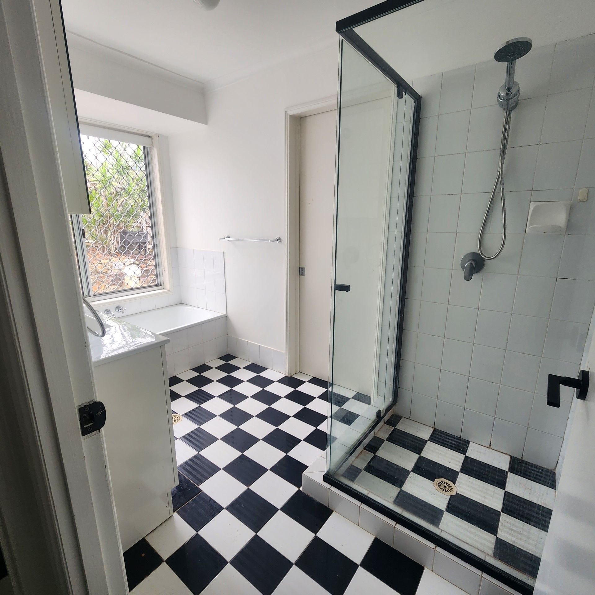A bathroom with a black and white checkered floor and a walk in shower