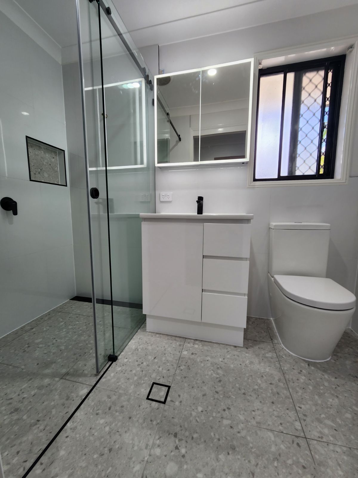 A bathroom with a toilet , sink , mirror and shower.