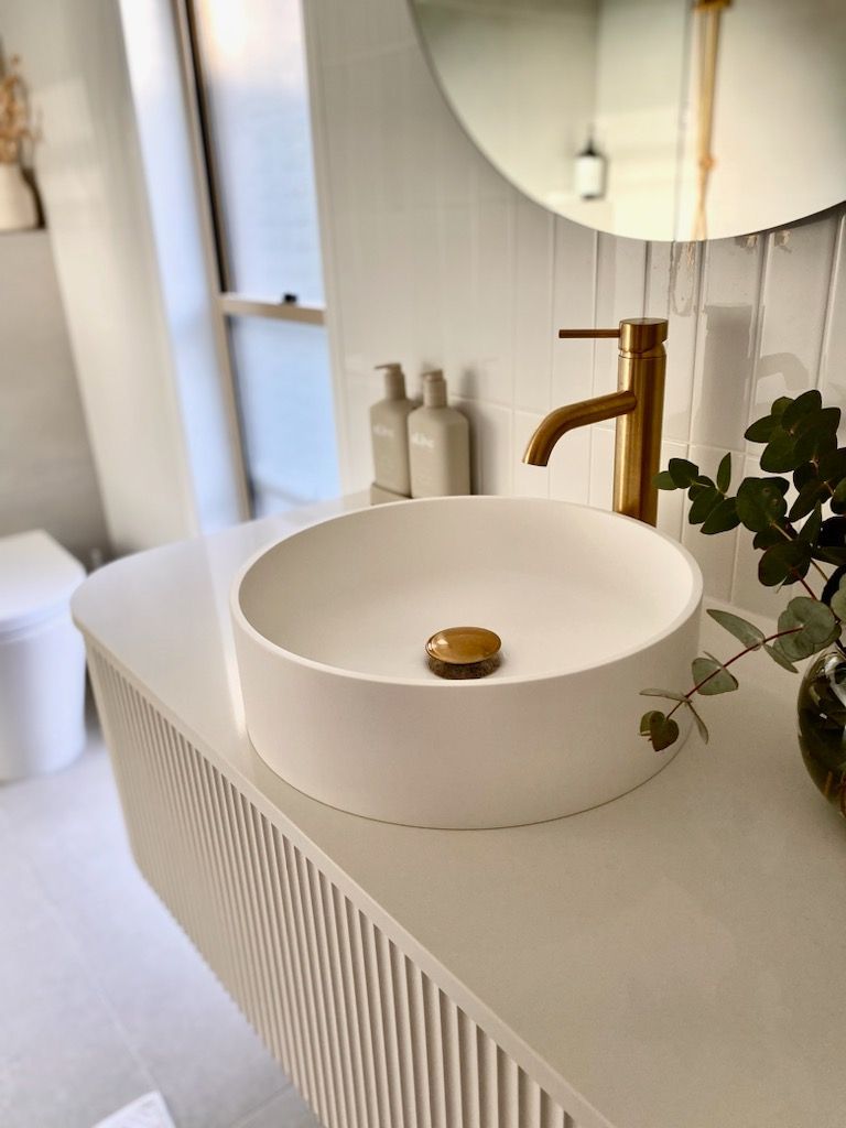 A bathroom with a round sink and a gold faucet.