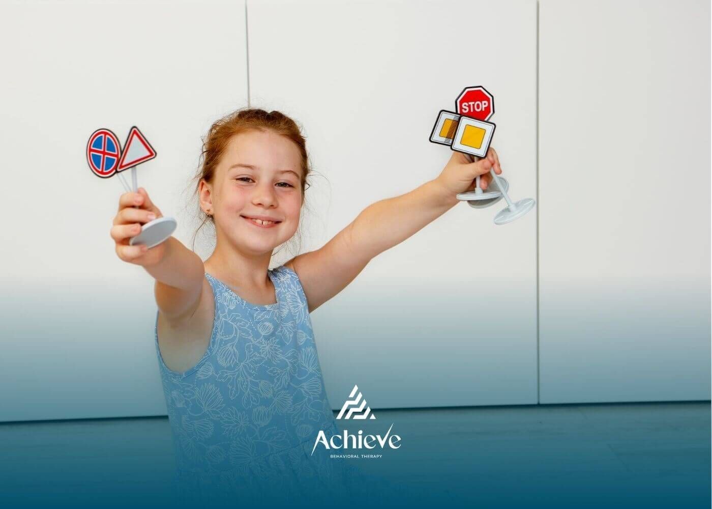 Young girl with autism smiling and holding up small toy traffic signs while sitting on the floor.