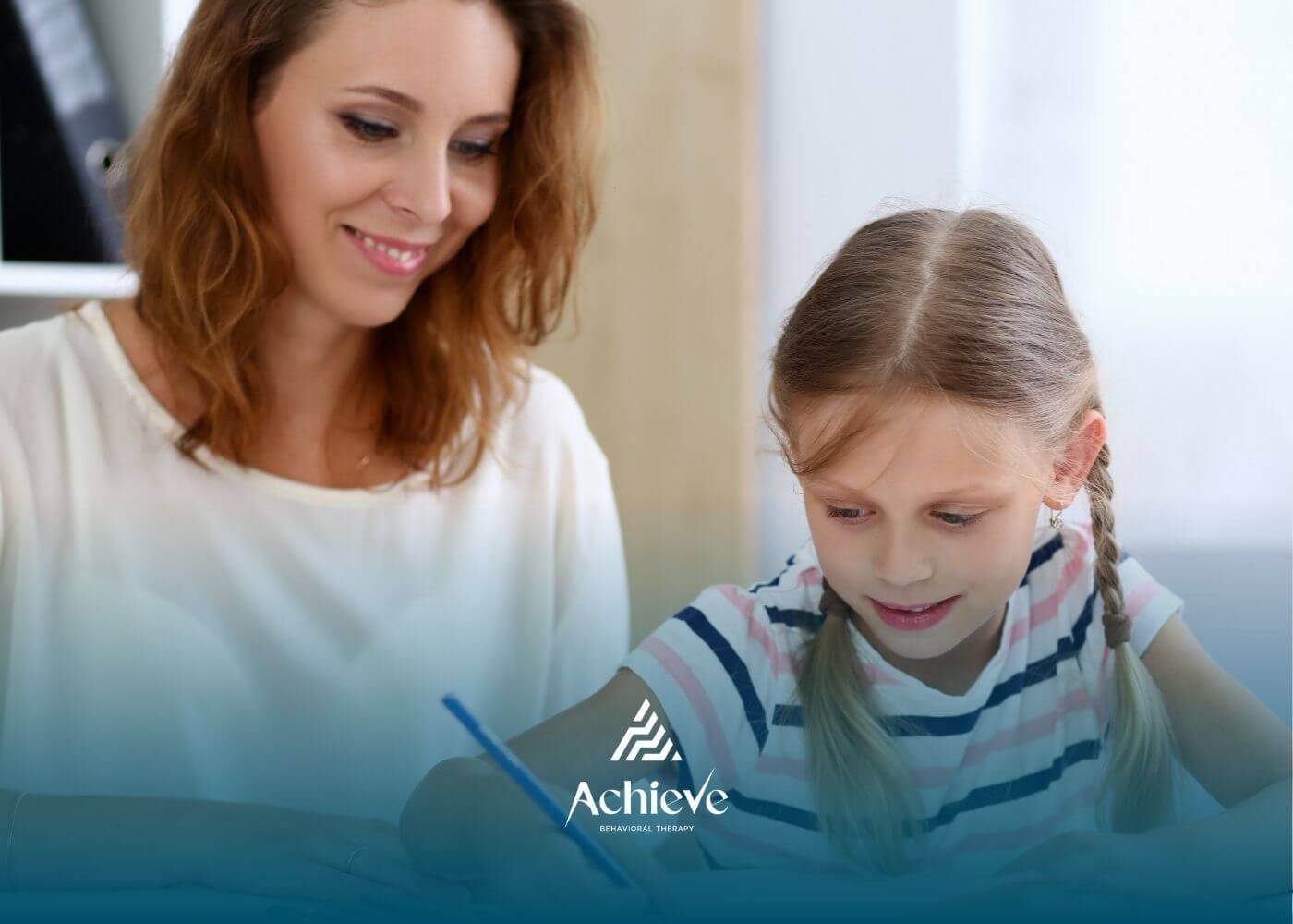 Female ABA therapist helping young girl with schoolwork at table in ABA therapy.