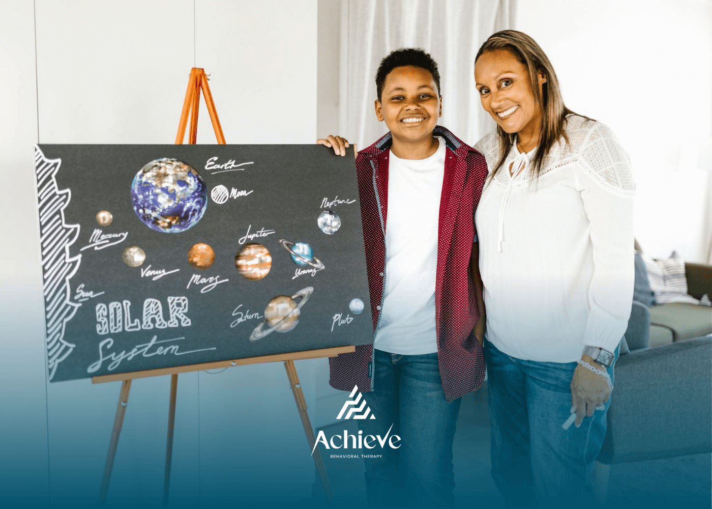 A BCBA and an autistic boy smiling beside the solar system project board during ABA therapy in NC.