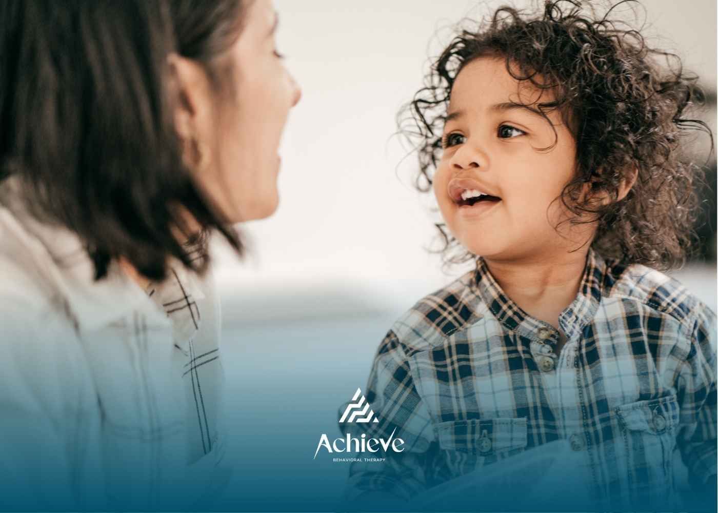 A happy child with curly hair in a plaid shirt looks up at an adult, creating a warm connection.