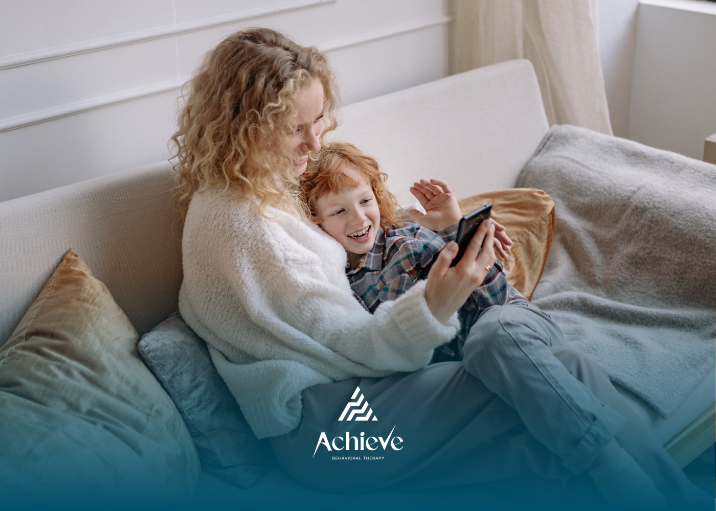 Parent and child relaxing on a couch, smiling at a smartphone in a cozy living room.