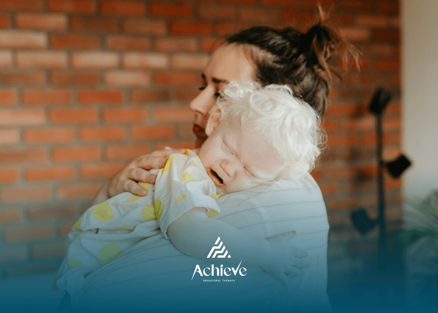 An ABA therapist comforting a crying autistic baby having a meltdown in her arms indoors in NJ.