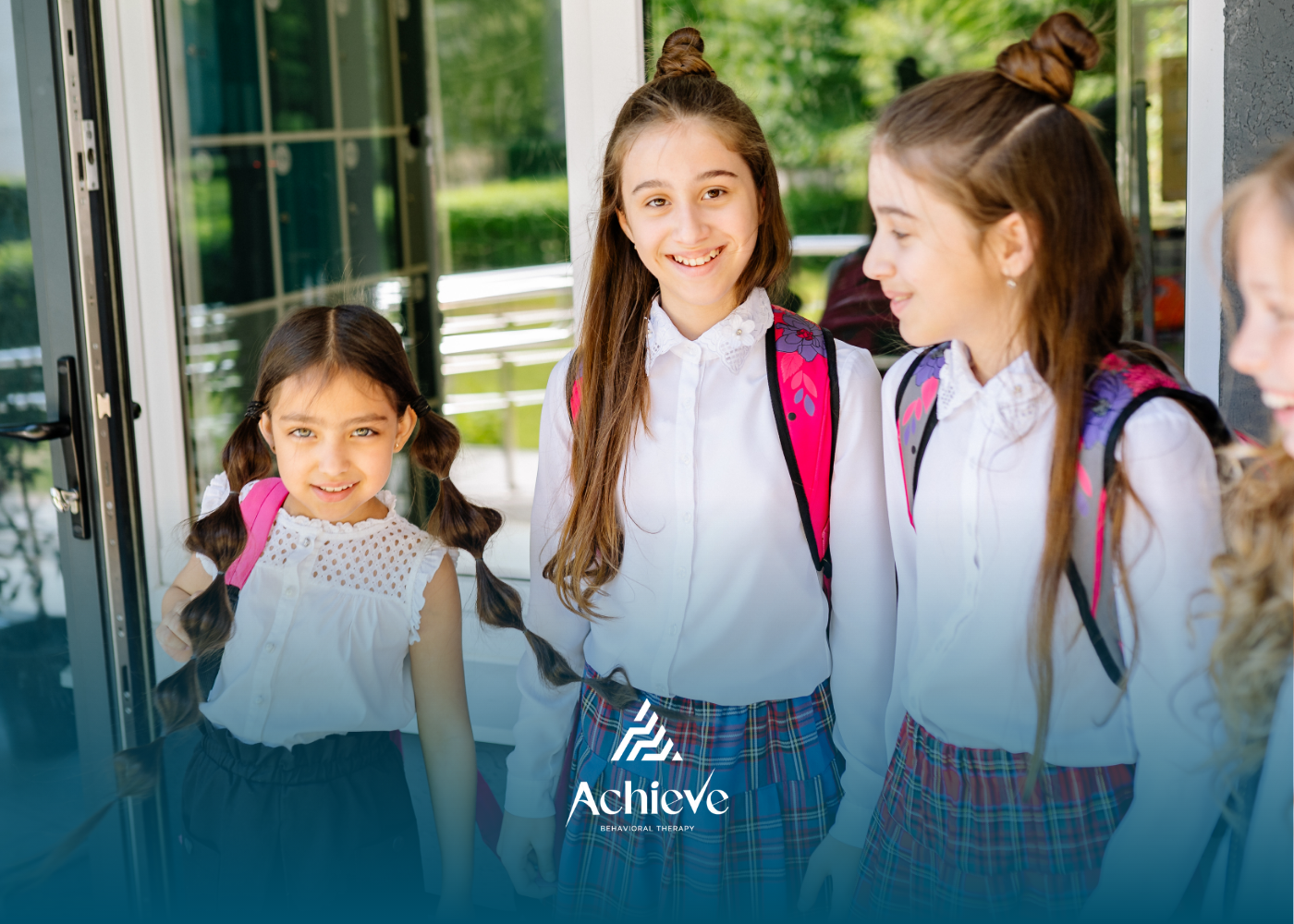 Three children with backpacks standing outside a building, smiling and chatting